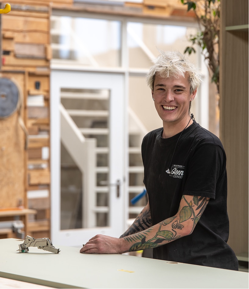 Meubelmaker Glenn glimlachend in zijn werkplaats tijdens de montage van interieur maatwerk